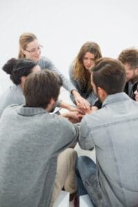 A group of people sitting in a circle, stacking their hands in the center as a gesture of support and unity.