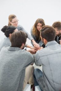 A group of people sitting in a circle, stacking their hands in the center as a gesture of support and unity.