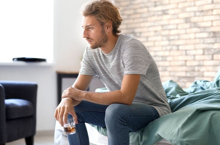 man sitting on a couch with a glass of liquor in his hand