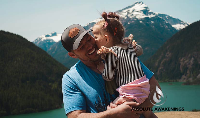 smiling man holding his daughter in front of a mountain range