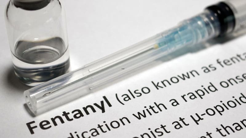A vial and syringe rest atop a document with the word 'Fentanyl' highlighted, discussing the medication's characteristics.