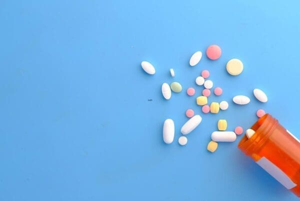 An assortment of colorful pills scattered from an orange pill bottle on a blue background.