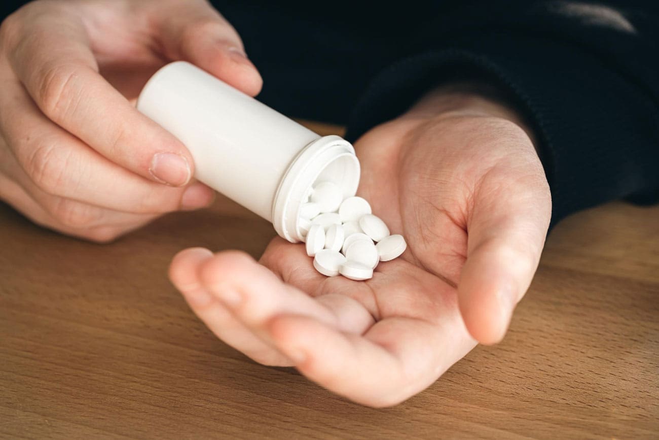 A person is pouring white pills from a bottle into their hand on a wooden surface.