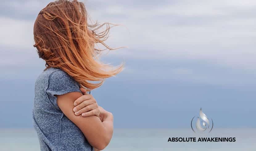 woman standing at the beach with her arms crossed while her hair blows in the wind
