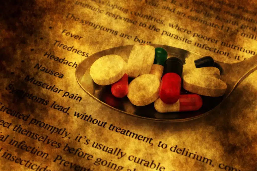 Spoon with various pills and capsules placed on medical text