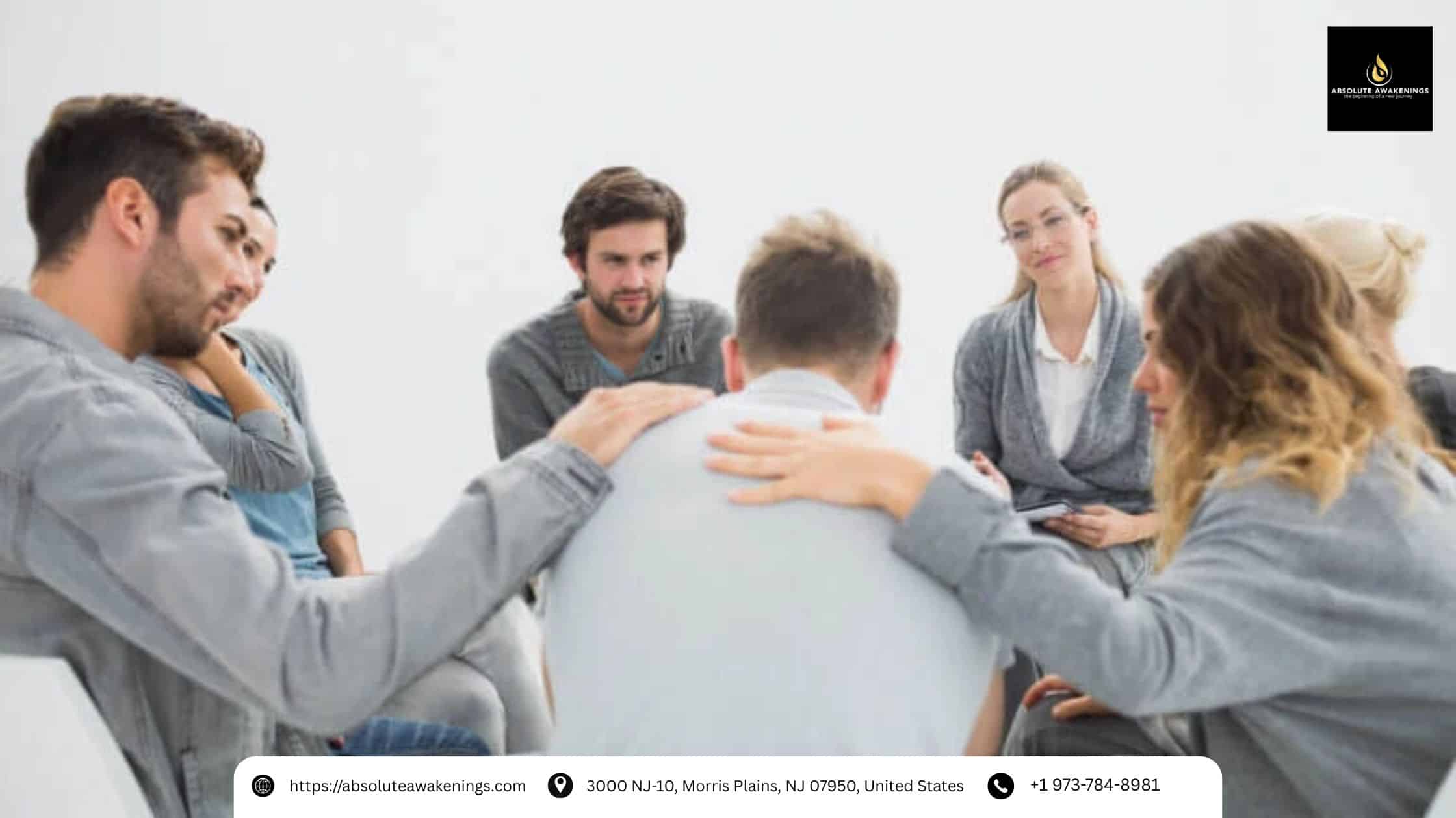A support group sitting in a circle, comforting a man by placing their hands on his shoulders.
